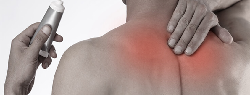 Rear view of a man rubbing his upper back and shoulder to soothe pain, holding a silver topical pain-relief cream tube in his hand, with a red glow highlighting the sore muscles.